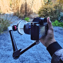 Load image into Gallery viewer, An intimate close-up shot of a photographer’s hand holding a camera that is equipped with the LLPLAB V4 Linear Prism Filter via a magic arm. This perspective showcases the practical, ready-to-shoot ergonomics of the setup, conveying both the stability of the mounted filter and the immediate creative control it offers.
